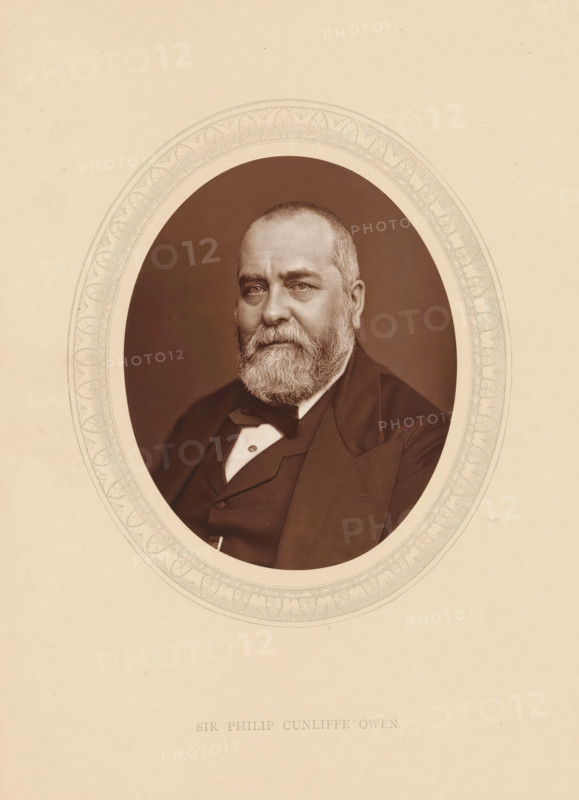 Sir Philip Cunliffe Owen, page, photomechanical print, photographer: Lock & Whitfield, cliché maker: anonymous, c. 1875 - in or before 1880, paper, Woodburytype, Woodbury Process, height 115 mm x width 89 mm, Person, Philip Cunliffe-Owen, director, boss (in modern industry), historical persons (portraits and scenes from the life) ((full) bust portrait), An oval portrait of an older man with a full beard and short hair set against a dark background, framed by a decorative oval border on a light-colored page, the man wearing a dark suit jacket with a vest and a bow tie, his gaze directed slightly forward and his expression neutral.