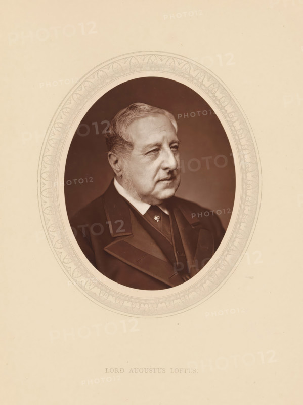 Lord Augustus Loftus, page, photomechanical print, photographer: Lock & Whitfield, cliché maker: anonymous, c. 1875 - in or before 1880, paper, Woodburytype, Woodbury Process, height 115 mm x width 89 mm, Person, Augustus Loftus, diplomacy, diplomat, historical persons (portraits and scenes from the life) ((full) bust portrait), A sepia-toned oval portrait of an older man shown from the chest up, facing slightly to the viewer's right, with short swept-back hair and sideburns, wearing a dark formal coat with wide lapels and a vest, set against a darker oval background framed by an ornate decorative border, all on a light beige mount.