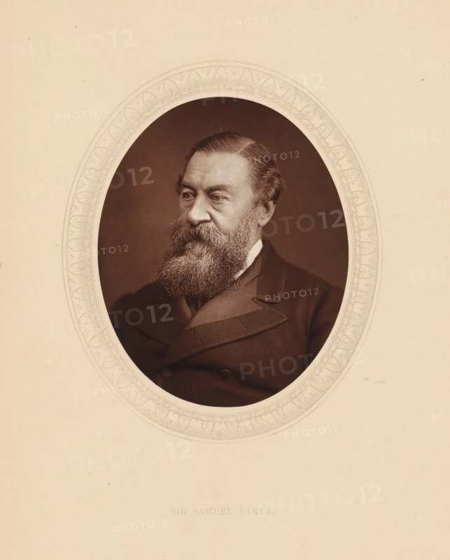 Sir Samuel Baker, page, photomechanical print, photographer: Lock & Whitfield, cliché maker: anonymous, c. 1875 - in or before 1880, paper, Woodburytype, Woodbury Process, height 115 mm x width 89 mm, Person, Samuel White Baker, explorer, historical persons (portraits and scenes from the life) ((full) bust portrait), A sepia-toned oval portrait of an older man with a full bushy beard and mustache, neatly combed hair, and a solemn expression, dressed in a dark formal coat with visible lapels, set against a plain dark background and surrounded by a decorative oval border on a light beige mount.