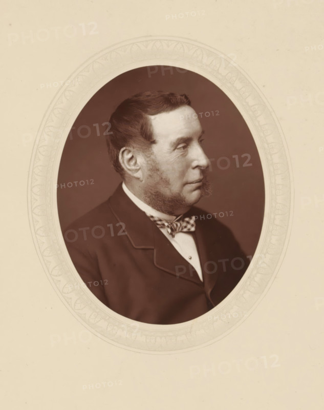 Right hon. Sir George Jessel, page, photomechanical print, photographer: Lock & Whitfield, cliché maker: anonymous, c. 1876 - in or before 1881, paper, Woodburytype, Woodbury Process, height 115 mm x width 89 mm, Person, George Jessel, magistracy, judges, historical persons (portraits and scenes from the life) ((full) bust portrait), A sepia-toned oval portrait of a man shown in profile facing right, with short dark hair and mutton chop sideburns, wearing a dark jacket with a notched lapel, a light shirt, and a patterned bow tie, set against a plain dark background and framed by an ornate pale oval mat with decorative border, all on a pale cream background.
