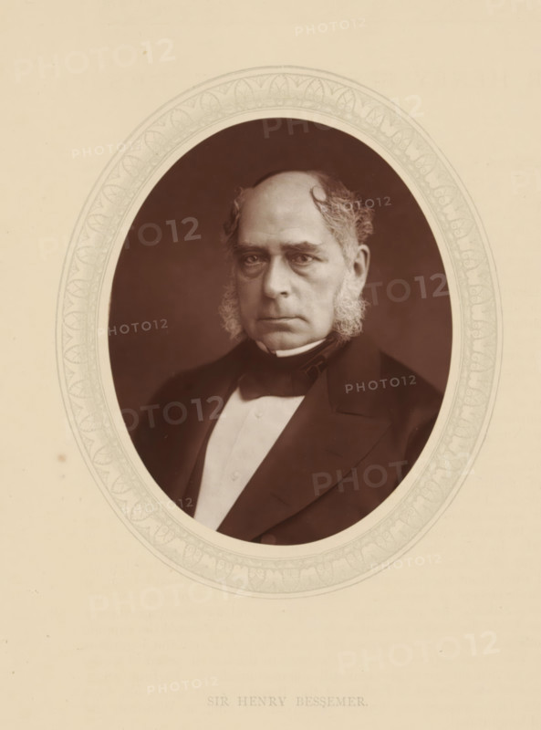 Sir Henry Bessemer, page, photomechanical print, photographer: Lock & Whitfield, cliché maker: anonymous, c. 1876 - in or before 1881, paper, Woodburytype, Woodbury Process, height 115 mm x width 89 mm, Person, Henry Bessemer, engineering, historical persons (portraits and scenes from the life) ((full) bust portrait), An oval sepia portrait of an older man with a high forehead and receding hairline, sideburns, and a serious expression, dressed in a dark coat, bow tie, and light waistcoat, set against a dark background and bordered by a decorative oval frame on a light beige background.