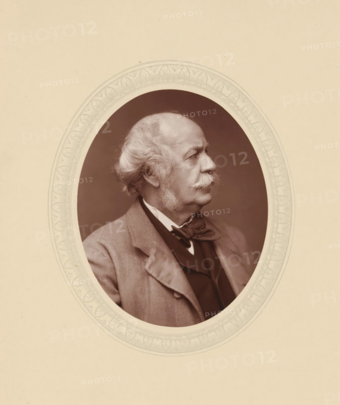Sir Henry Creswicke Rawlinson, page, photomechanical print, photographer: Lock & Whitfield, cliché maker: anonymous, c. 1877 - in or before 1882, paper, Woodburytype, Woodbury Process, height 115 mm x width 89 mm, Person, Henry Rawlinson, scholar, philosopher, historical persons (portraits and scenes from the life) ((full) bust portrait), A sepia-toned oval portrait of an older man shown in profile facing right, with a receding hairline and wavy white hair at the sides, prominent sideburns and a thick moustache, wearing a jacket over a vest and a bow tied at the collar; the oval image is set within a decorative light-colored frame with a patterned border against a plain light background.