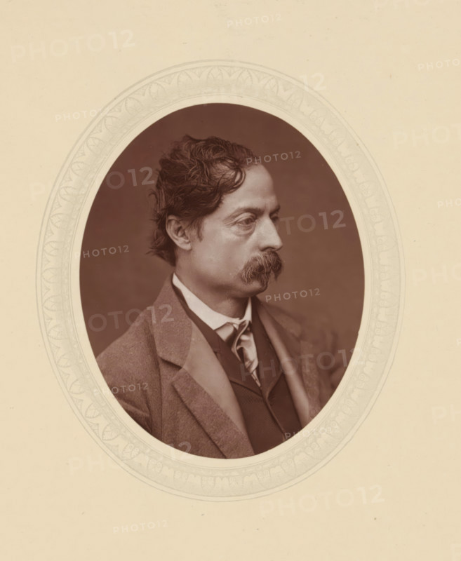 William Quiller Orchardson, page, photomechanical print, photographer: Lock & Whitfield, cliché maker: anonymous, c. 1877 - in or before 1882, paper, Woodburytype, Woodbury Process, height 115 mm x width 89 mm, Person, portrait, self-portrait of painter, historical persons (portraits and scenes from the life) ((full) bust portrait), An oval sepia photograph of a man shown in profile facing right, with wavy dark hair and a full mustache, wearing a collared shirt, tie, waistcoat, and an overcoat, set against a plain dark background and surrounded by a decorative light-colored oval mat with a patterned border on a neutral page.