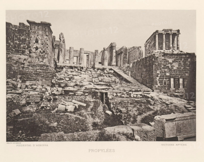 Propylées, View of the Propylées of the Acropolis of Athens, page, photomechanical print, inscription: 'Piedestal d'Agrippa Victoire aptère', Athens, cliché maker: Dujardin, printer (person): Chardon-Wittmann, c. 1880 - in or before 1890, Dujardin, Chardon-Wittmann, photographer, cliché maker, printer (person), Athene, Periféreia Protevoúsis, paper, photoaquatint, height 145 mm x width 215 mm, ruin of a building, architecture, gate, entrance, staircase, Acropolis, Propylaea (Athens), A wide monochrome photograph shows an ancient stone entrance with a broad flight of worn steps leading upward through rubble and scattered carved blocks toward a row of weathered columns and lintels at the top; flanking the steps are massive stone walls and terraces built of irregular blocks, with a small rectangular opening in the foreground wall and remnants of broken architectural elements strewn across the uneven ground; on the right a raised platform supports a small colonnaded structure with slender ...
