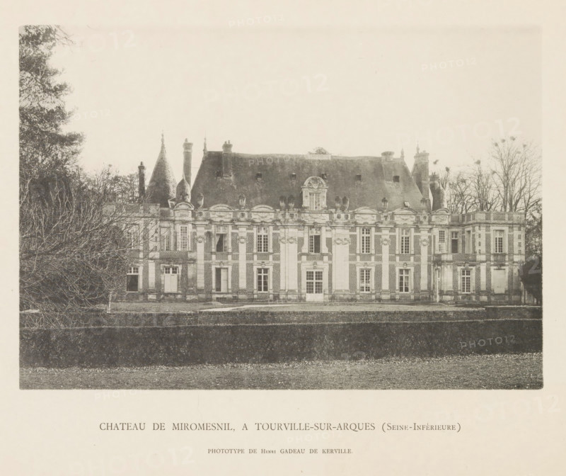 Exterior of the Castle of Miromesnil in Tourville-sur-Arques, Chateau de Miromesnil, a Tourville-sur-Arques (Seine-Inférieure), page, photomechanical print, number: 'Pl. IV.', photographer: Henri Gadeau de Kerville, Tourville-sur-Arques, cliché maker: Raoul Bonet (possibly), c. 1885 - in or before 1895, paper, collotype, phototype, height 141 mm x width 205 mm, castle, façade (of house or building), Miromesnil Castle, A wide frontal view of a large historic stone building with a steep slate roof, ornate chimneys, and decorative rooftop sculptures, framed on either side by bare trees and dense shrubbery, with a darker foreground lawn and a low retaining wall separating the building from the nearer ground.
