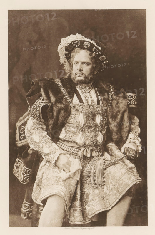 William Terriss (Henry VIII), page, photomechanical print, cliché maker: Swan Electric Engraving Co., c. 1880 - in or before 1890, photographer, paper, photoaquatint, height 211 mm x width 131 mm, Person, portrait of actor, actress, A seated man wearing an ornate costume with heavy embroidery, beading, and layered fabrics is shown from head to knees. He has a wreathlike hat decorated with lace and jewels, curly hair, and a full beard and mustache. A fur-trimmed cloak drapes over his shoulders and a richly decorated tunic with patterned sleeves and a sash with tassels covers his torso and hips. His hands rest on his lap, one holding a cloth, and he wears patterned knee breeches. The background is plain and dark.