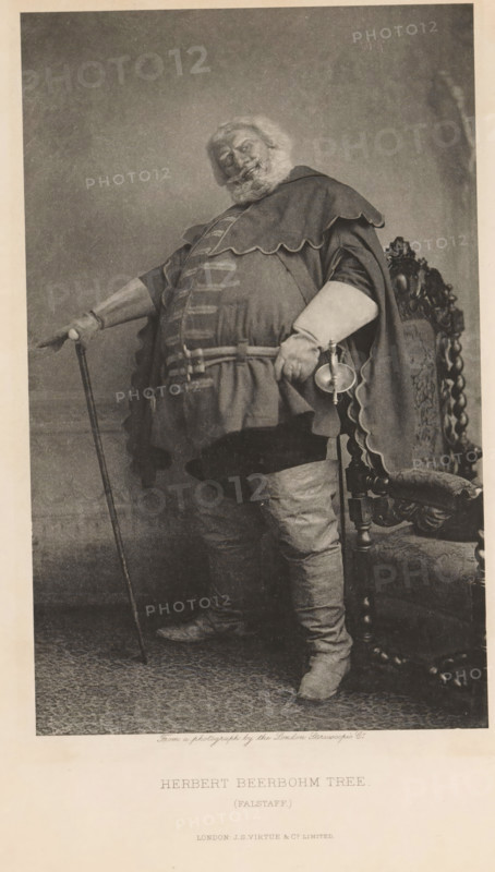 Herbert Beerbohm Tree (Falstaff), page, photomechanical print, photographer: London Stereoscopic Company, cliché maker: anonymous, publisher: Virtue & Co., c. 1880 - in or before 1890, paper, photoaquatint, height 208 mm x width 129 mm, Person, portrait of actor, actress, A full-length portrait of a heavyset older man standing beside an ornately carved chair, wearing a layered costume with a scalloped cape, long sleeves, and a belted tunic, with a bushy beard and hair, one hand resting on a cane and the other holding a small cup and a short sword at his side, high boots covering his legs, a patterned floor beneath him, and a plain backdrop behind him.