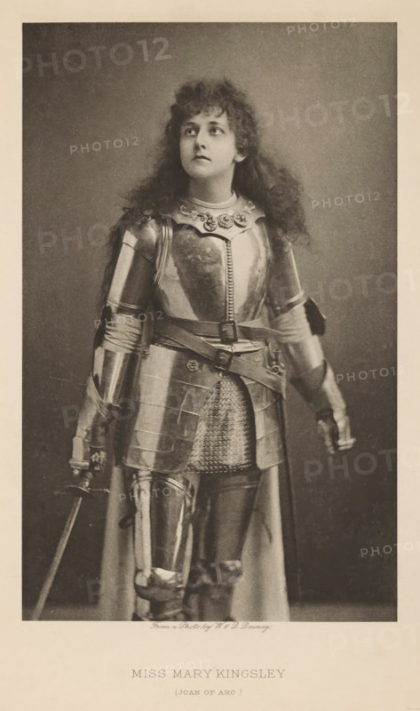 Miss Mary Kingsley (Joan of Arc), page, photomechanical print, photographer: Downey, William & Daniel, cliché maker: anonymous, publisher: Virtue & Co., London, c. 1880 - in or before 1890, paper, photoaquatint, height 197 mm x width 123 mm, Person, Mary Kingsley, portrait of actor, actress, A sepia-toned portrait of a person wearing a full suit of metal armor, including a breastplate with decorative elements at the neckline, articulated shoulder and arm pieces, gauntlets, a belted waist with metal plates over a chainmail apron, and greaves over the legs; the person has long, curly hair and is looking upward and slightly to the side with a neutral facial expression, one hand resting near the hilt of a sword and the other hanging by the side, the background is plain and darker than the subject, and the image has a lighter border around it.