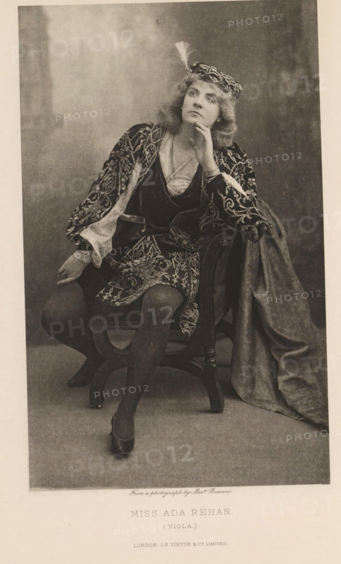 Miss Ada Rehan (Viola), page, photomechanical print, photographer: Alexander Bassano, cliché maker: anonymous, publisher: Virtue & Co., London, c. 1880 - in or before 1890, paper, photoaquatint, height 196 mm x width 122 mm, Person, Ada Rehan, portrait of actor, actress, A seated woman in a patterned costume with ornate embroidery and flowing sleeves looks upward with a hand resting against her chin, wearing a decorative cap with a feather and textured hair; she sits on a carved wooden chair with one leg crossed over the other, dark stockings and shoes visible, while a heavy draped fabric falls beside the chair and a soft, mottled backdrop fills the frame.