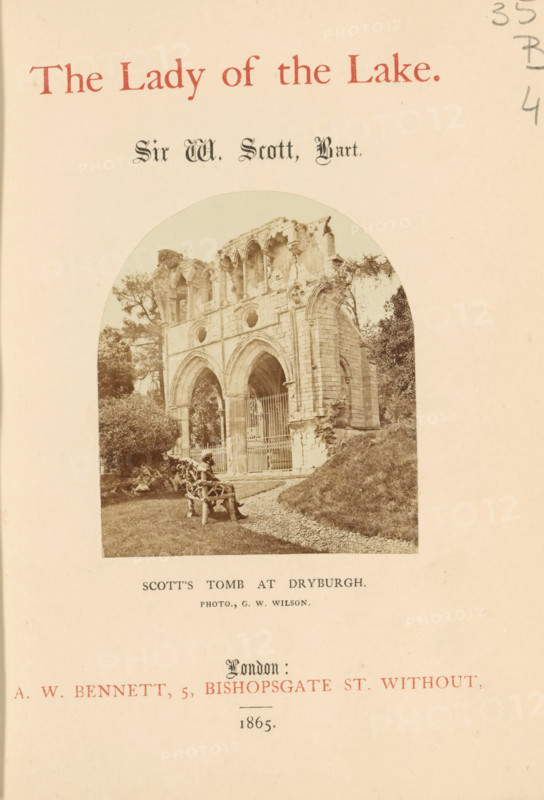 Walter Scott's grave at Dryburgh Abbey, Scott's tomb at Dryburgh, photograph, page, photographer: George Washington Wilson, Dryburgh Abbey, c. 1855 - in or before 1865, paper, albumen print, height 79 mm x width 69 mm, Photo on title page., Person, Walter Scott, grave, tomb, A faded book page showing a sepia photograph of a ruined stone façade with tall arched openings and circular window openings, set within an arched frame; a gravel path and grassy bank lead toward the structure, a sculpted wooden bench sits on the lawn in front with a small pile of stones nearby, trees and shrubbery appear behind and beside the ruins, and decorative printed headings appear above and below the photograph.