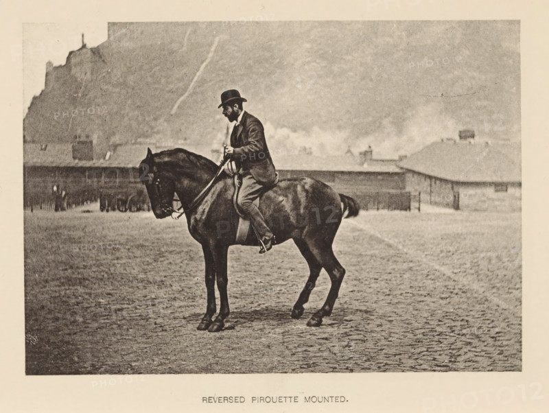 Man on horseback, Reversed pirouette mounted, page, photomechanical print, photographer: Alexander Nicol (possibly), Edinburgh (possibly), cliché maker: Römmler & Jonas, Dresden, c. 1879 - in or before 1889, paper, collotype, photoprint, height 97 mm x width 137 mm, horse, riding a horse, ass, or mule, rider, horseman, head-gear: bowler hat, A sepia-toned scene shows a man wearing a dark suit and bowler hat seated on a dark horse in a cobblestone open area, the man holding reins and looking downward; behind them are low buildings with pitched roofs and chimneys, and in the distant background a rocky hillside rises with a structure silhouetted near its top.