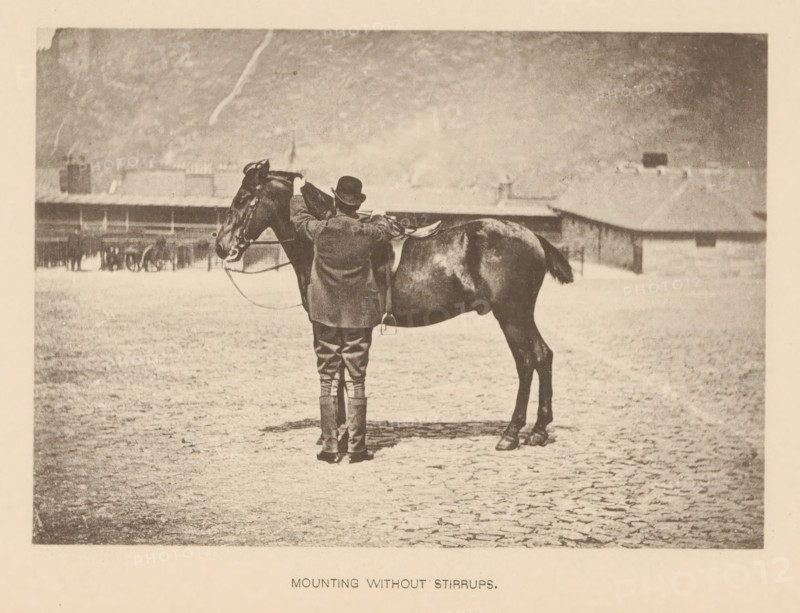 Mounting without Stirrups, Man mounting a horse without using the stirrups, page, photomechanical print, cliché maker: Römmler & Jonas, Dresden, c. 1879 - in or before 1889, photographer, paper, collotype, photoprint, height 96 mm x width 137 mm, horse, riding a horse, ass, or mule, rider, horseman, head-gear: bowler hat, A sepia-toned photograph shows a person standing behind a saddled horse in an open, flat area with a textured ground. The person wears a hat, a long coat, riding breeches, and high boots, and their hands rest on the horse's neck near the saddle. The horse faces left with visible bridle and reins, a shiny coat, and a tucked tail. In the background there are low buildings and a distant hillside under a pale sky.