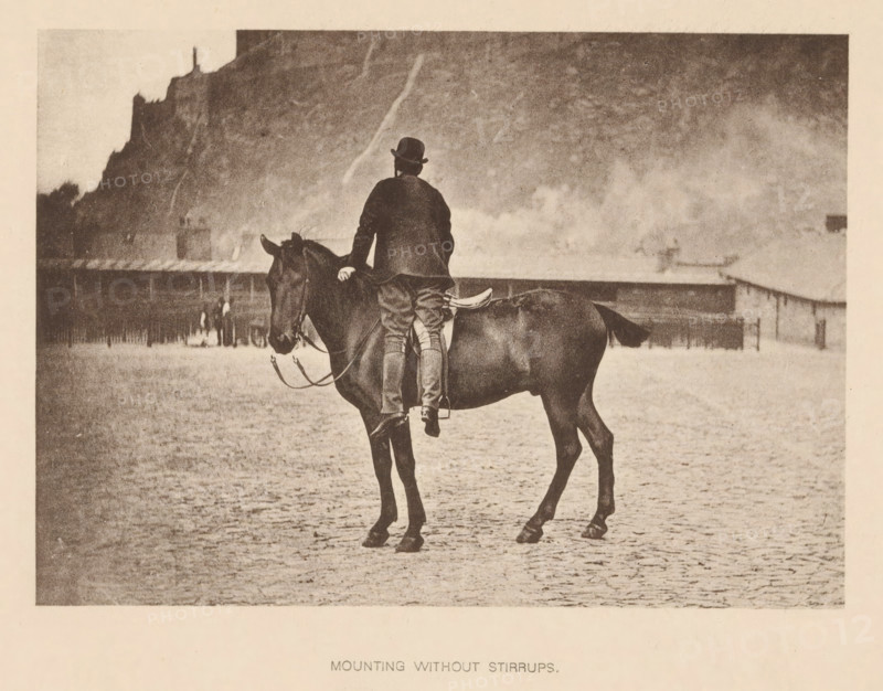 Mounting without Stirrups, Man mounting a horse without using the stirrups, page, photomechanical print, cliché maker: Römmler & Jonas, Dresden, c. 1879 - in or before 1889, photographer, paper, collotype, photoprint, height 97 mm x width 137 mm, horse, riding a horse, ass, or mule, rider, horseman, head-gear: bowler hat, A sepia-toned photograph shows a person wearing a dark coat and a rounded hat sitting on a dark horse viewed from behind, with one hand resting on the horse's neck and legs visible without stirrups, the horse standing on a textured ground in front of a distant low building and a steep cliff rising behind it, with a hazy sky above.