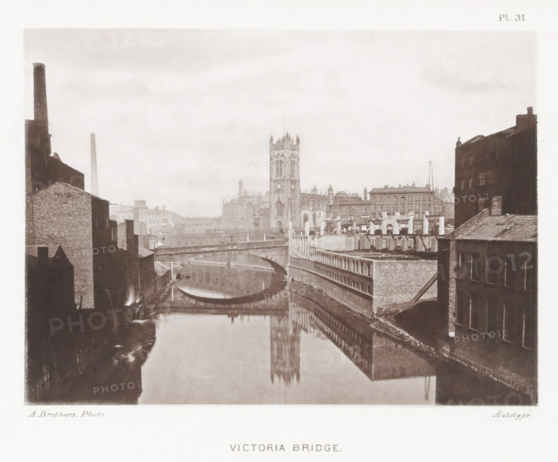 Victoria Bridge, View of the Victoria Bridge over the Irwell in Manchester, page, photomechanical print, number: 'Pl. 31.', photographer: Brothers, Alfred, Manchester, cliché maker: anonymous, c. 1868 - in or before 1878, printer (person), paper, collotype, photoprint, height 138 mm x width 188 mm, Print after page 30., bridge in city across river, canal, tower, clock tower, monumental adornment, A sepia-toned cityscape showing a river flanked by brick buildings with a stone bridge arching across the water and reflecting in the river, industrial chimneys and rooftops visible on either side, a tall Gothic church tower rising in the center background with its reflection mirrored in the water, and rows of buildings and architectural details lining the riverbank under an overcast sky.
