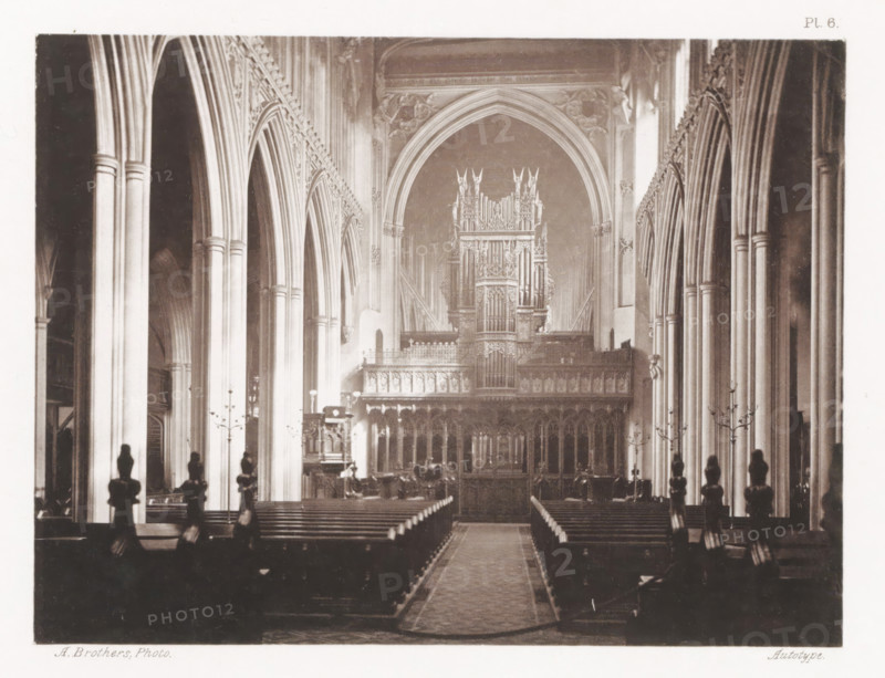 The Cathedral. Nave, Interior of the nave of Manchester Cathedral, page, photomechanical print, number: 'Pl. 6.', photographer: Brothers, Alfred, Manchester, clichémaker: anonymous, c. 1868 - in or before 1878, printer (person), paper, collotype, photogravure, height 139 mm x width 184 mm, parts of church interior: nave, Manchester Cathedral, A long, narrow interior view of a cathedral nave with tall pointed arches and clustered columns lining both sides, a central aisle carpet leading toward an ornate carved choir screen and a large pipe organ set within a pointed arch at the far end, wooden pews arranged in rows on either side of the aisle, decorative stone tracery and sculpted details along the upper walls and arches, tall metal candelabra standing beside the pews, and silhouetted finials or carved figures visible atop the ends of the pews in the foreground.