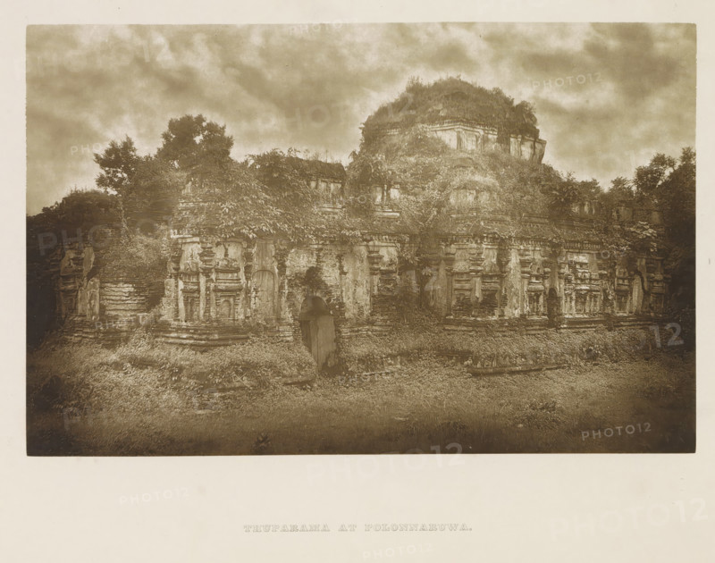 Ruins of the Thuparama temple at Polonnaruwa, Sri Lanka, page, photomechanical print, title: 'THUPARAMA AT POLONNARUWA.', photographer: Henry William Cave, Polonnaruwa, cliché maker: anonymous, 1896, South Asia, paper, Woodburygravure, height 124 mm x width 193 mm, Print for page 113., temple, shrine, Hinduism, Buddhism, Jainism, ruin of a building, architecture, A sepia-toned photograph of an ancient stone structure partially covered by vegetation, showing weathered carved facades with recessed niches and decorative moldings, a central arched doorway, and layered stone terraces; plants and vines grow over many surfaces and trees rise behind and above the structure under a cloudy sky.
