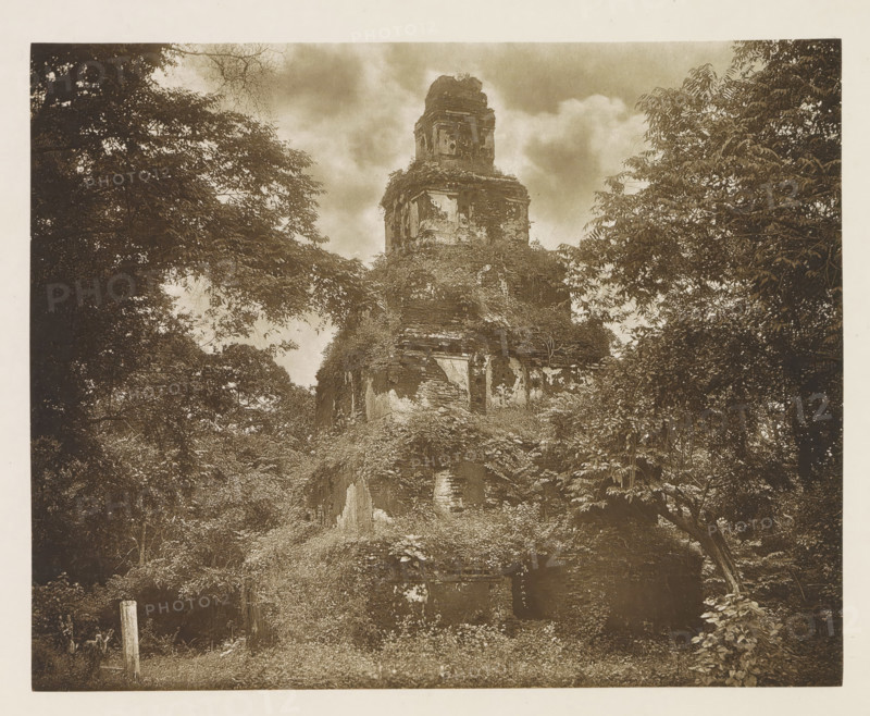 Ruins of the Satmahal Prasada stupa at Polonnaruwa, Sri Lanka, page, photomechanical print, title: 'SAT-MAHAL-PRASADA.', photographer: Henry William Cave, Polonnaruwa, cliché maker: anonymous, 1896, South Asia, paper, Woodburygravure, height 147 mm x width 184 mm, Print for page 117., temple, shrine, Hinduism, Buddhism, Jainism, ruin of a building, architecture, A tall, weathered stone structure covered in vines and vegetation rises from a grassy, overgrown foreground, its crumbling surfaces showing patches of exposed brick and eroded plaster; the ruin is framed by dense trees with layered foliage on both sides and branches extending toward the center, and a cloudy sky fills the background above the structure.