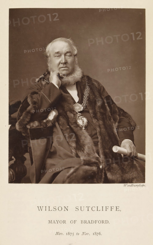 Portrait of Wilson Sutcliffe, Wilson Sutcliffe, mayor of Bradford, page, photomechanical print, inscription: 'Nov. 1875 to Nov. 1876.', photographer: Appleton & Co., Bradford (England), cliché maker: anonymous, c. 1871 - in or before 1881, paper, Woodburytype, height 116 mm x width 91 mm, historical persons (portraits and scenes from the life), A sepia portrait of an older man seated and facing forward, wearing a dark formal robe trimmed with fur and a heavy decorative chain with a large medallion visible on his chest, his left hand resting on his cheek and his right hand holding a cylindrical object, he has a full beard and short hair, and there is a plain neutral backdrop behind him.