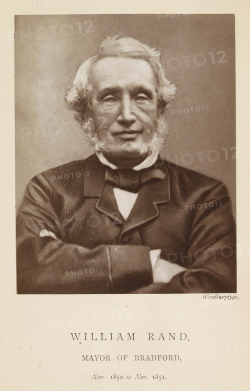 William Rand, mayor of Bradford, Portrait of William Rand, page, photomechanical print, inscription: 'Nov. 1850 to Nov. 1851.', photographer: Appleton & Co., Bradford (England), cliché maker: anonymous, c. 1871 - in or before 1881, paper, Woodburytype, Woodburytypepie, height 116 mm x width 91 mm, historical persons (portraits and scenes from the life) ((full) bust portrait), A sepia-toned portrait of an older man shown from the chest up, facing forward with arms folded across his torso; he has light-colored hair styled with waves at the sides and mutton chops framing his face, a smooth forehead, gentle eyes, and a neutral expression; he wears a dark formal jacket with a high collar and a bow at the neck, a light shirt peeking through the jacket opening, and the image is bordered by a light margin.