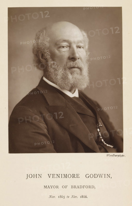John Venimore Godwin, mayor of Bradford, Portrait of John Venimore Godwin, page, photomechanical print, inscription: 'Nov. 1865 to Nov. 1866.', photographer: Appleton & Co., Bradford (England), cliché maker: anonymous, c. 1871 - in or before 1881, paper, Woodburytype, height 117 mm x width 92 mm, Person, historical persons (portraits and scenes from the life) ((full) bust portrait), A sepia-toned portrait of an older man shown from the chest up, facing slightly to the viewer's left, with a bald head and a full curly beard and mustache, wearing a dark suit jacket over a vest and a white collar, a watch chain visible on the vest, set against a plain backdrop and framed by a light border.