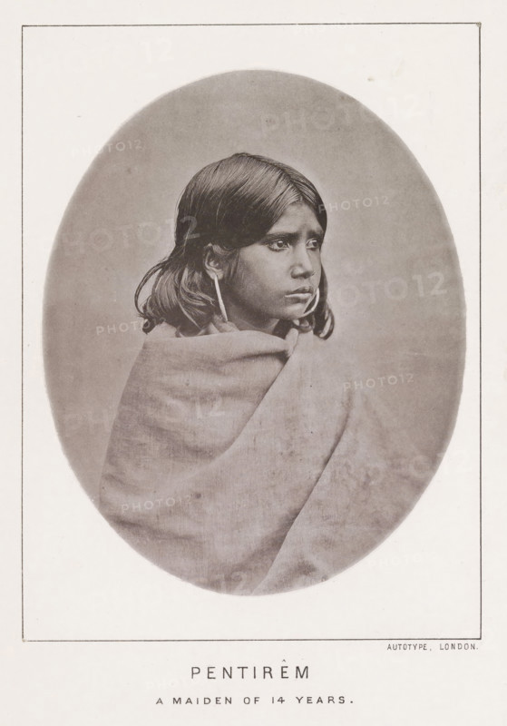 Pentirêm a maiden of 14 years, page, photomechanical print, number: 'No. 24', photographer: Bourne & Shepherd, Nilgiris, photographer: Nicholas & Curths, cliché maker: anonymous, printer (person): Autotype Printing Company, London, c. 1863 - in or before 1873, printer (person), paper, collotype, photoprint, height 121 mm x width 98 mm, adolescent, young woman, maiden, A sepia-toned oval portrait of a young person wrapped in a blanket, shown from the chest up and turned slightly to the side, with straight dark hair falling to shoulder length, large round earrings, and a neutral facial expression, set against a plain background and surrounded by a rectangular page border.