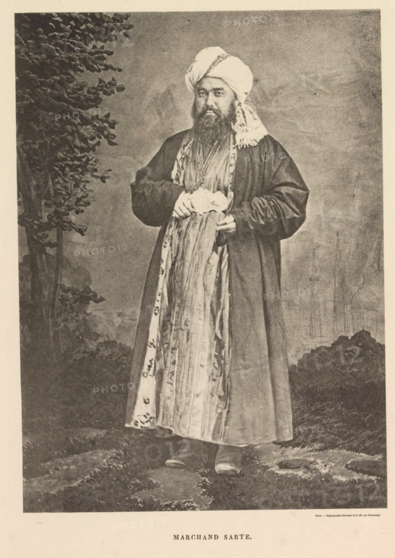 Portrait of a merchant of Sart descent, Marchand Sarte, page, photomechanical print, name: 'Silvestre et Cie, 97, rue Oberkampf.', Central Asia, cliché maker: anonymous, printer (person): Silvestre et Cie, Paris, c. 1875 - in or before 1885, photographer, printer (person), paper, collotype, photoprint, height 175 mm x width 128 mm, merchant, salesman, A full-length portrait of a bearded man standing outdoors in front of a shaded backdrop, wearing a long dark robe over a patterned inner garment and a long decorative scarf that hangs down the front, his hands clasping a folded cloth at waist level, a turban wrapped around his head with a fringed cloth draped over one shoulder, foliage visible to one side and low vegetation underfoot, with a lightly textured sky behind him.