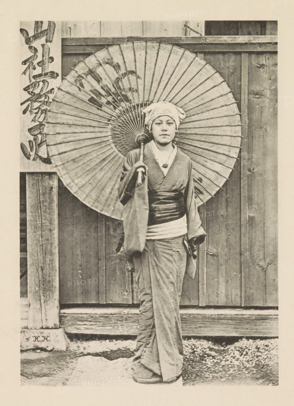 Jeune fille japonaise, Girl with a parasol in Japan, page, photomechanical print, inscription: 'HK', inscription: 'Photographie de l'autoriteit.', photographer: Hugues Krafft, Japan, cliché maker: anonymous, in or after 1882 - in or before 1883, Hugues Krafft, photographer, cliché maker, paper, collotype, photoprint, height 173 mm x width 122 mm, Photo opposite title page., folk costume, regional costume, child, parasol, sunshade, A person standing in front of a wooden wall holding a large paper umbrella behind their head, wearing a headscarf and traditional robe with a wide sash, with visible folds and texture in the fabric and a neutral facial expression, the umbrella showing radial ribs and a darker circular center, wooden posts and planks framing the scene and a gravelly ground beneath the person.