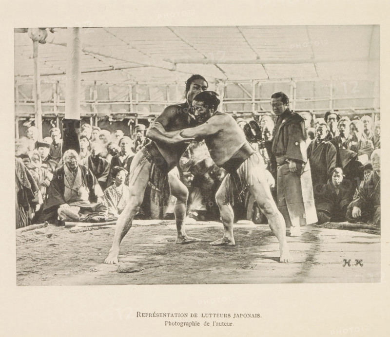 Représentant de lutteurs japonais, Sumo wrestling match in Tokyo, page, photomechanical print, inscription: 'HK', inscription: 'Photographie de l'autoriteit.', photographer: Hugues Krafft, Tokyo, cliché maker: anonymous, in or after 1882 - in or before 1884, Hugues Krafft, photographer, cliché maker, Kanto, paper, collotype, light printing, height 122 mm x width 172 mm, fighting contest (sport), wrestling (sport), Two shirtless men wearing traditional loincloths are grappling in a ring, their arms locked around each other and their bodies tensed; one man faces slightly toward the camera while the other looks past him. A crowd of spectators surrounds the ring, many seated and wearing robes, with varied facial expressions and postures; a man in darker clothing stands near the ring holding an object. The setting shows a covered structure with visible posts and a ceiling grid, and the ground inside the ring appears textured and worn.