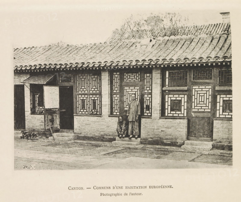 Part of the facade of a house in Canton, Canton. - Communs d'une habitation Européenne, page, photomechanical print, inscription: 'Photographie de l'autoriteit.', inscription: 'HK', photographer: Hugues Krafft, Canton (city), cliché maker: anonymous, in or after 1882 - in or before 1883, paper, collotype, photoprint, height 122 mm x width 169 mm, housing, facade (of house or building), A monochrome photograph of a traditional building facade with a tiled roof and decorative lattice windows shows two men in front of a doorway; one man stands on a small stone step wearing loose clothing and the other crouches beside him. The roof features curved tiles and a ridge line, with some foliage visible behind it. The building walls are made of brick with wooden window frames and patterned geometric lattice panels. A small porch area with an open shuttered window and a leaning wooden ladder or board is visible to one side, and the paved courtyard in front shows worn stone slabs and a low raised t...