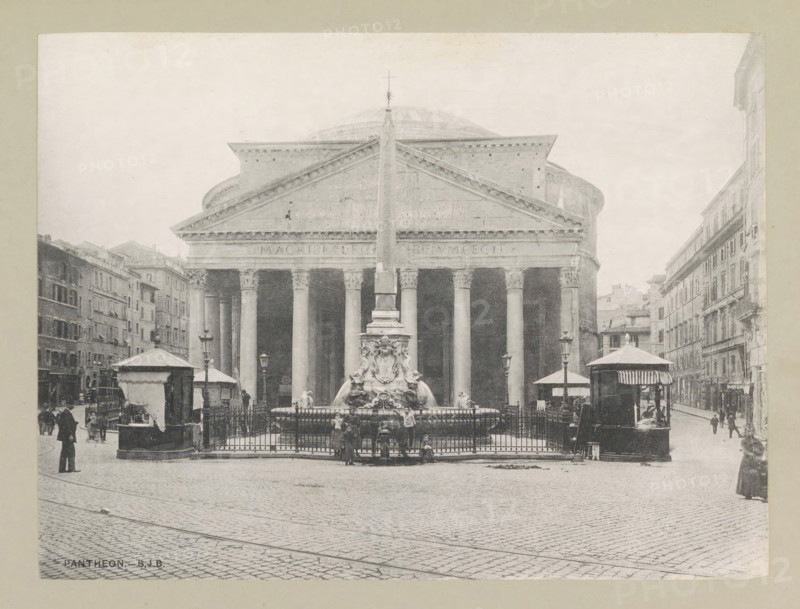 Pantheon, page, photomechanical print, photographer: Samuel J. Beckett, Piazza della Rotonda, c. 1890 - c. 1900, Rome, paper, collotype, photoprint, height 152 mm x width 203 mm, church (exterior), facade (of house or building), A grayscale photograph of a large classical building with a triangular pediment and a row of tall columns across its facade, a dome visible behind the pediment, and an obelisk rising from the center in front of the building; a sculpted fountain with ornamental figures sits at the base of the obelisk, enclosed by a metal fence; flanking the fountain are small kiosk-like structures with awnings and street lamps, and multi-story buildings line the streets on both sides of the plaza; cobblestone pavement fills the foreground and a few people stand or walk near the fountain and along the street.