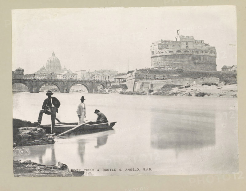River Tiber & Castle S. Angelo, page, photomechanical print, photographer: Samuel J. Beckett, Rome, c. 1890 - c. 1900, paper, collotype, photoprint, height 152 mm x width 203 mm, rowing-boat, canoe, landscape with bridge, viaduct or aqueduct, river, Tiber, Engelenburcht, A wide grayscale scene shows a riverside with a stone bridge spanning the water and a large cylindrical fortress on the far bank, its upper walls and rooftop structures visible. A domed building and a row of low buildings appear behind the bridge. In the foreground three men and a small rowboat are at the river edge; one man stands on a rock with one foot raised, another stands in the boat wearing a hat, and a third is seated in the boat leaning forward. Reflections of the figures and the boat are visible in the smooth water. The image has a light, slightly faded tone and a pale border around the edges.