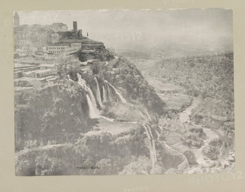 Tivoli, page, photomechanical print, photographer: Samuel J. Beckett, c. 1890 - c. 1900, paper, collotype, photoprint, height 153 mm x width 202 mm, city-view in general, 'veduta', waterfall, A grayscale photograph showing a cliffside town with clustered buildings and a prominent tower near the top, terraced slopes and a winding road along the cliff edge, cascading waterfalls flowing down rock faces into a river below, scattered trees and vegetation across the hillside and valley, cultivated plots and pathways visible in the lower landscape, and a hazy distant plain extending toward the horizon.