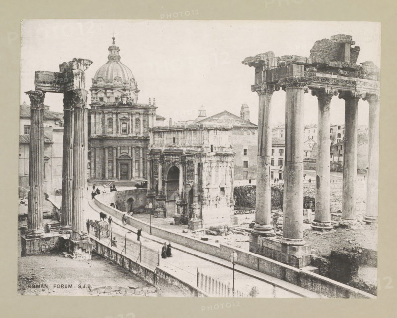 Roman Forum, page, photomechanical print, photographer: Samuel J. Beckett, Forum Romanum, c. 1890 - c. 1900, Rome, paper, collotype, photoprint, height 150 mm x width 194 mm, landscape with ruins, facade (of house or building), A sepia-toned photograph shows a view of ancient stone columns and ruins adjacent to a large domed building with ornate façade details and sculptural elements; tall fluted columns with carved capitals stand in the foreground beside a curving raised walkway with a railing and lamp posts, where small groups of people are walking or standing; the ruins include archways, layered stone blocks, and fragmented entablatures, while in the background there are multi-story masonry buildings with windows and simple rooflines.