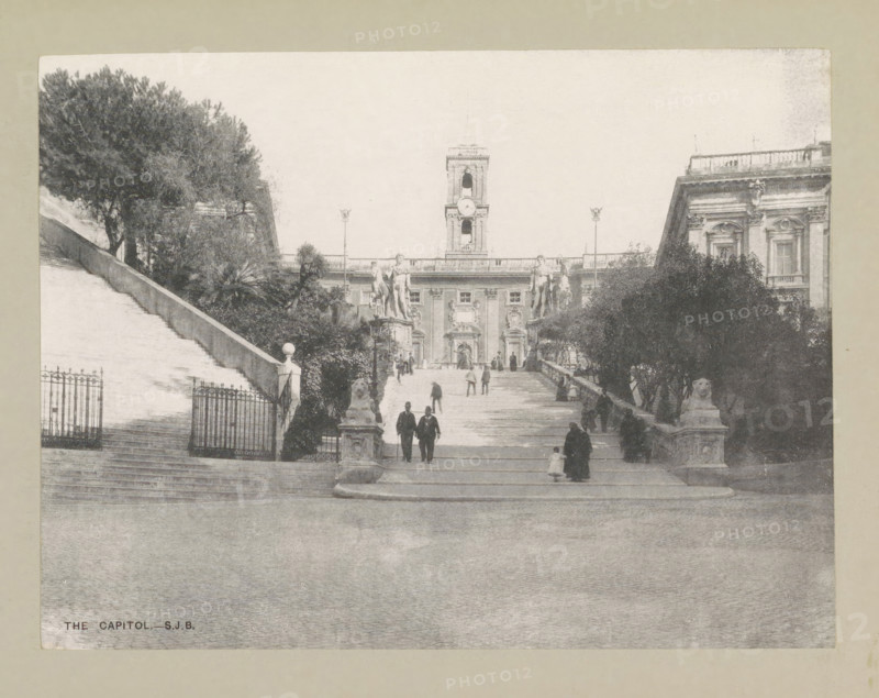 The capitol, page, photomechanical print, photographer: Samuel J. Beckett, Rome, c. 1890 - c. 1900, paper, collotype, photoprint, height 152 mm x width 202 mm, square, circus, staircase, Piazza del Campidoglio, A wide stone staircase leads up to a large classical building with a central clock tower and ornate façades, flanked by statues of figures on pedestals and lamp posts; trees and bushes line the sides of the stairs, and wrought iron gates and stone balustrades are visible near the lower landings; several people in period clothing are walking up and down the steps, including pairs and single figures, while sculpted lion figures sit on plinths at the base of the stairs.