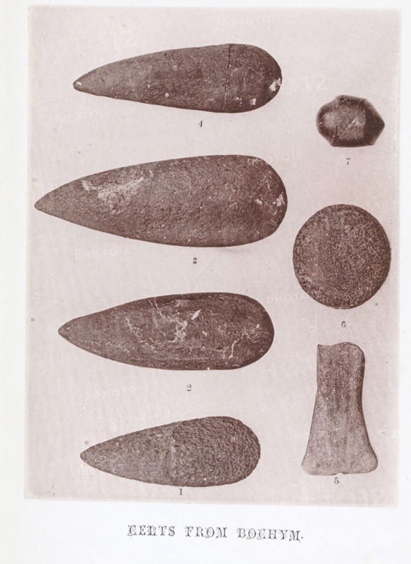 Celts from Bochym, page, photomechanical print, number: '1, 7', photographer: Beringer, Cury, c. 1870 - in or before 1875, printmaker, Cornwall, paper, collotype, photoprint, height 108 mm x width 143 mm, casting weapons: spear, A vertical page shows a pale background with several dark, textured stone objects arranged in two vertical columns, the left column containing elongated, teardrop-shaped stones with rounded wider ends and tapered points, each showing surface irregularities and lighter mottled patches, and the right column containing a round, flat disc-like stone, a small irregularly faceted pebble, and a roughly rectangular stone with a narrowed middle and flared base, all depicted with granular textures and worn edges.