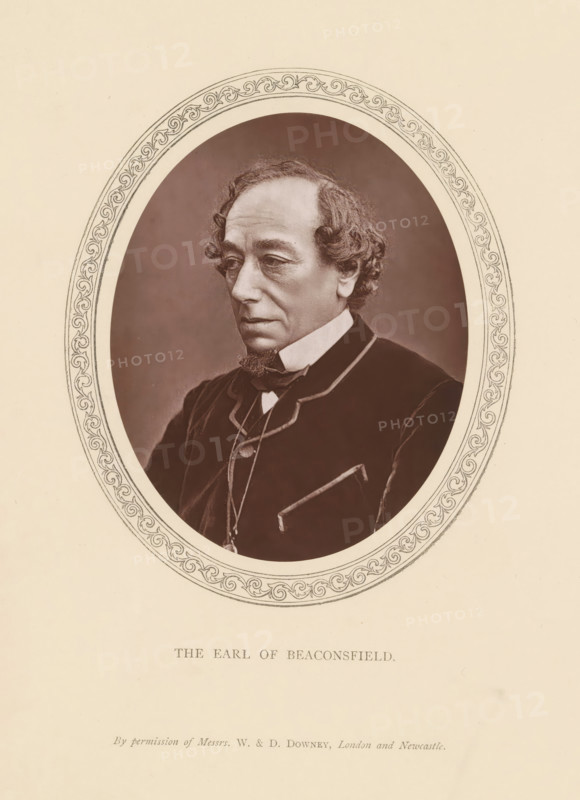 The Earl of Beaconsfield, page, photomechanical print, photographer: Downey, William & Daniel, London, c. 1869 - in or before 1881-04-19, printmaker, paper, Woodburytype, height 116 mm x width 93 mm, Person, Benjamin Disraeli, politician, eg party leader, An oval-framed sepia portrait of an older man shown from the chest up wearing a dark coat with a high white collar and a bow at the neck, his hair curly at the sides and receding at the top, a small pointed beard on his chin, a thoughtful expression with downcast eyes, set against a plain darker oval background and surrounded by an ornate border on a light paper page.