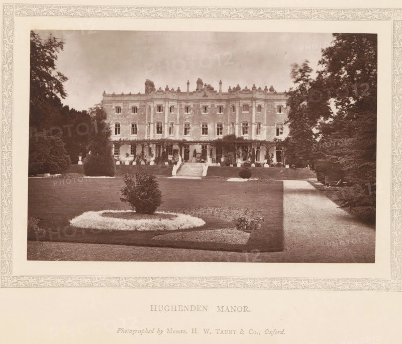 Hughenden manor, page, photomechanical print, photographer: Henry W. Taunt, High Wycombe, c. 1876 - in or before 1881, printmaker, Buckinghamshire, paper, Woodburytype, height 96 mm x width 145 mm, rural housing, eg country-house, villa, cottage, A sepia-toned photograph of a large three-story brick manor centered in a landscaped garden, flanked by tall trees on both sides, with an expansive lawn and gravel path in the foreground; the manor shows rows of windows, a veranda with climbing plants, a central stairway leading up to an entrance, decorative roofline features and chimneys, sculpted shrubs and a circular flowerbed on the lawn, and several potted plants near the path.