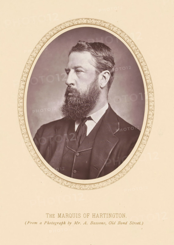 Portrait of Spencer Cavendish, The marquis of Hartington, page, photomechanical print, photographer: Alexander Bassano, London, c. 1877 - c. 1882, printmaker, paper, Woodburytype, height 111 mm x width 87 mm, Person, Spencer Cavendish, politician, eg party leader, A sepia-toned oval portrait of a bearded man in a dark suit and tie set against a plain background, framed by an ornate oval border, with the man shown in three-quarter profile facing left and wearing a jacket with visible lapels and a high-collared shirt.