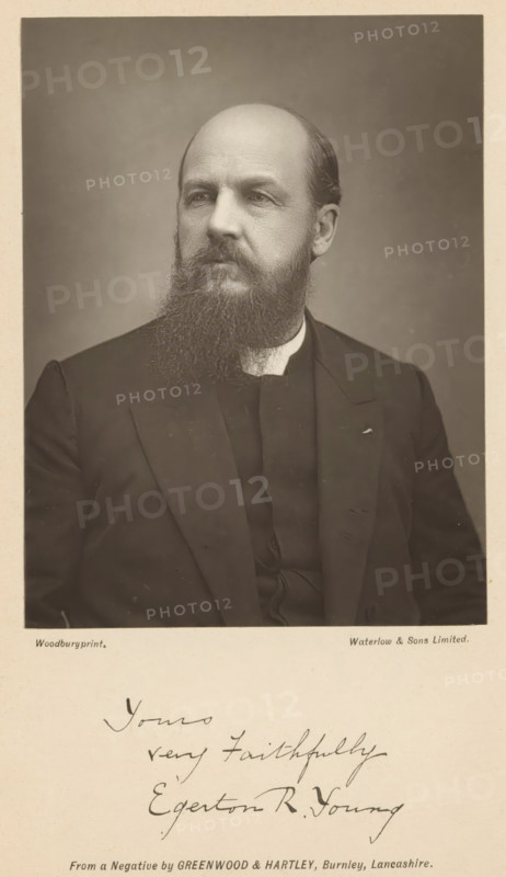 Portrait of Egerton Ryerson Young, page, photomechanical print, inscription: 'Yours very faithfully Egerton R. Young', photographer: Greenwood & Hartley, maker: Waterman, c. 1882 - in or before 1892, paper, Woodburytype, height 117 mm x width 88 mm, Print opposite title page., Person, Egerton Ryerson Young, adult man, spreading the gospel, missionary work, A sepia portrait of a seated man shown from the chest up against a plain background, with a high forehead and a full beard and mustache, wearing a dark suit jacket over a dark vest and a light collar, his head turned slightly to his left and his gaze directed off camera, the image framed by a light border with handwritten script visible below the portrait.