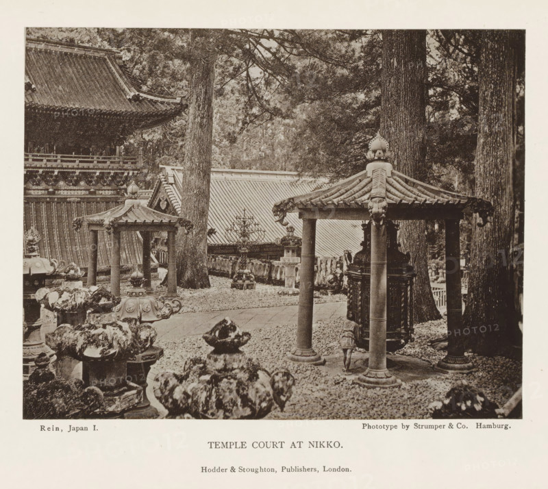 Temple court at Nikko, page, photomechanical print, Nikko, printmaker: Strumper & Co, Hamburg (city), publisher: Hodder & Stoughton, London, c. 1874 - in or before 1884, photographer, Kanto, paper, collotype, photoprint, height 117 mm x width 151 mm, facade of inner court, temple, shrine, Shinto, A sepia-toned photograph showing an outdoor scene with traditional East Asian temple architecture and stone lanterns among tall trees, featuring a tiled pavilion roof supported by cylindrical columns in the foreground and ornate carved details on roof edges and lantern tops, uneven stone and gravel ground with scattered rocks and ornamental bases, large tree trunks rising behind the structures, a larger building with a steep tiled roof and decorative eaves partially visible in the background, and various sculptural elements and carved wooden or stone fixtures arranged throughout the courtyard.
