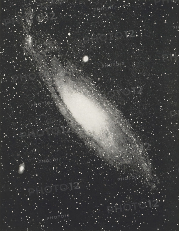Great nebula in Andromeda, page, photomechanical print, inscription: 'Photographed by, Miss Herschel in 1783.', photographer: Isaac Roberts, 1888-12-29, printmaker, paper, autotypie, height 131 mm x width 100 mm, astronomical phenomena, A rectangular black-and-white image of a star-filled sky centered on an elongated, bright nebulous shape with a dense bright core and a tapered outer region, surrounded by numerous small bright points on a dark background and a few slightly larger circular bright spots.