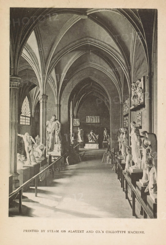 Image gallery, page, photomechanical print, printmaker: Alauzet & Co. (possibly), c. 1877 - in or before 1887, photographer, printer (person), paper, collotype, printed by steam, height 143 mm x width 102 mm, gallery of sculptures, exterior, representation of a building, A long vaulted interior with pointed ribbed arches and tall columns framing a central aisle lined on both sides with sculpted figures on pedestals and relief panels mounted on the walls, sunlight casting shadows across the floor from a tall arched window on the left, a bench or railing running along the aisle edges, and distant statues and a raised platform visible at the far end.