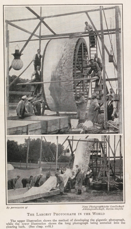 Developing and washing a large panoramic photograph on a roll, The largest photograph in the world, page, photomechanical print, inscription: 'The upper illustration shows the method of developing the gigantic photograph, while the lower illustration shows the long photograph being unreeled into the clearing bath. (See chap. xviii.)', photographer: Neue Photographische Gesellschaft, c. 1898 - in or before 1908, printmaker, paper, autotype, height 192 mm x width 120 mm, Prints opposite title page., photographic apparatus, A tall wooden frame supports a large cylindrical drum with a textured surface being worked on by several men; some men stand on ladders and platforms around the drum while others stand or kneel on the ground nearby, and a few men wear aprons or coats. A hanging lamp with a patterned globe is suspended from the frame on one side. Wooden beams, ropes, and pulley elements are visible around the structure. In the lower portion a long sheet is being unrolled or handled by a...