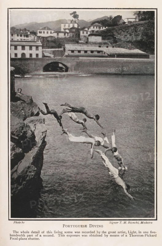 Portuguese diving, Boys diving off a cliff in Madeira, page, photomechanical print, inscription: 'The whole detail of this living scene was recorded by the great artist, Light, in one five-hundredth part of a second. This exposure was obtained by means of a Thornton-Pickard Focal-plane shutter.', photographer: TM Bianchi, Madeira, c. 1898 - in or before 1908, printmaker, paper, autotypie, height 136 mm x width 95 mm, diving (movement in water), A vertical black-and-white photograph showing several people mid-dive off a rocky cliff into a body of water, captured in successive positions forming an arc from the cliff edge down toward the water surface; the divers wear light-colored shorts or garments and are bare-chested, with limbs extended in diving poses; the rocky cliff appears on the left with jagged edges and a small metal ring attached near the top; the water fills the right and lower parts of the image with a textured surface; in the background across the water there is a stone em...