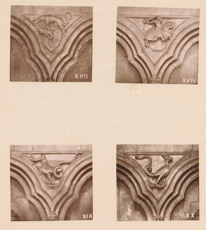 Four woodcarvings in an arcade of Worcester Cathedral, page, photomechanical print, Top left a griffin fighting an animal, top right a knight on horseback, bottom left a mythical creature, bottom right a basilisk., number: 'XVII, XX', c. 1863 - in or before 1873, paper, Woodburytype, Woodburytypie, height 305 mm x width 244 mm, interior of church, griffin (lion, eagle), 'Griffo' (Ripa), carving, applied arts, basilisk (cock with posterior of snake), Four rectangular sepia-toned photographs arranged in a grid show close-up views of carved stone architectural panels. Each photograph centers on a V-shaped grooved molding meeting at a carved boss. The top left panel features a stylized animal with a curved tail perched above the molding, its body elongated and limbs gripping the carved surface. The top right panel shows a figure wearing flowing garments leaning forward above the V-shaped molding, one arm extended. The bottom left panel depicts an animal with a curled tail and a raised fore...