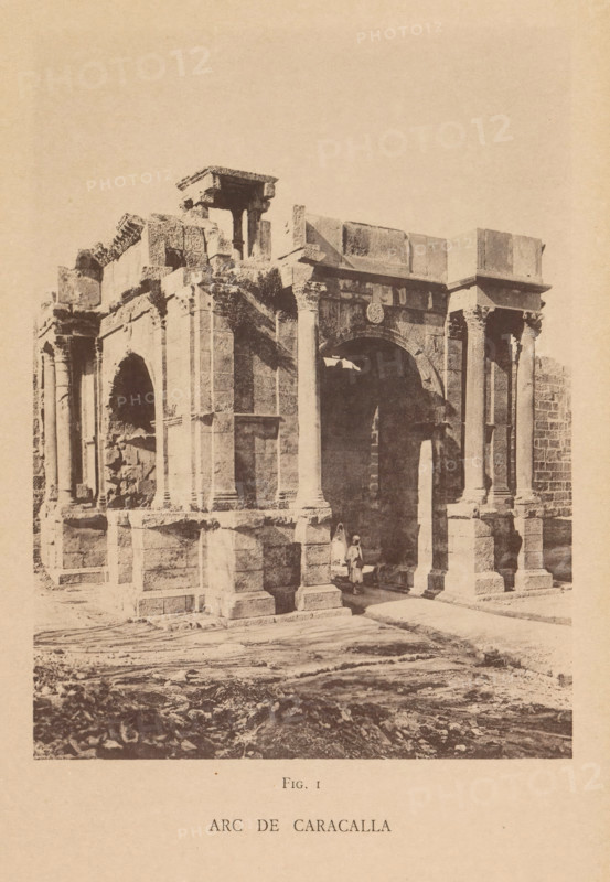 Arc de Caracalla, View of the Arch of Caracalla in Tébessa, page, photomechanical print, number: 'Fig. I', Tébessa, maker: Berthaud Frères, France, c. 1884 - in or before 1894, photographer, North Africa, paper, collotype, photoprint, height 148 mm x width 109 mm, triumphal arch, A sepia-toned photograph shows a large stone archway structure with tall columns and carved architectural details; the stone surfaces appear weathered and some sections are broken or crumbling. Two figures stand beneath the arch, one wearing a long garment and the other shorter, positioned near the shadowed interior. The foreground shows a rough, uneven ground with scattered stones and tracks, and the background above the structure is an empty sky.