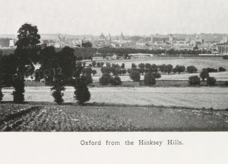 Oxford from the Hinksey Hills, page, photomechanical print, inscription: ''That sweet city with her dreaming spires.'', maker: Henry W. Taunt, Oxfordshire, c. 1907 - in or before 1912, paper, autotype, height 79 mm x width 132 mm, winter landscape, landscape symbolizing winter (the four seasons of the year), Oxford, A vertical black and white photograph of a landscape is visible on the left side, showing trees, fields, and distant buildings with a skyline; the photograph has a narrow white border and is rotated ninety degrees. The rest of the image shows a book page with closely spaced printed lines of text occupying the right side and lower portion, and a visible center gutter where the pages meet. The overall tones are grayscale with paper textures and slight shadows along the page crease.