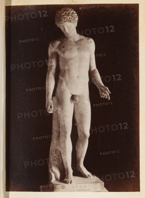 Capitoline Antinous in the Capitoline Museums, photograph, page, Rome, c. 1850 - in or before 1860, photographer, paper, albumen print, height 135 mm x width 98 mm, piece of sculpture, reproduction of a piece of sculpture, Capitoline Museums, A monochrome photograph of a full-length classical marble statue of a standing nude male figure shown from head to feet, positioned against a dark background with a lighter border; the figure has curly hair, a slightly tilted head, a relaxed posture with one arm hanging down and the other extended outward with the hand open, visible musculature and anatomical details, a support draped behind one leg, and bare feet resting on a rectangular base.