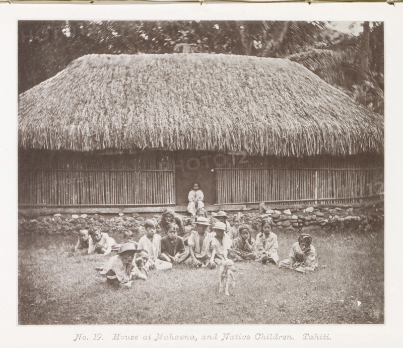 House at Mahaena, and Native Children.Tahiti, House in Mahaena with children from Tahiti in front of it, page, photomechanical print, number: 'No. 19.', photographer: Henry Stuart-Wortley, Tahiti, cliché maker: Meisenbach's Autotype Company, printer (person): Meisenbach's Autotype Company, 1880, Meisenbach's Autotype Company, photographer, French Polynesia, paper, collotype, photoprint, height 138 mm x width 166 mm, housing, child (at home), A large thatched roof hut fills the upper portion of the image with dense, straw-like material hanging over a structure of vertical wooden slats and a raised stone foundation, a narrow doorway at the center where a seated figure is visible, and in front of the building a group of people sit and recline on grass, some wearing wide-brimmed hats and loose clothing, with a small dog standing on the grass closer to the camera.