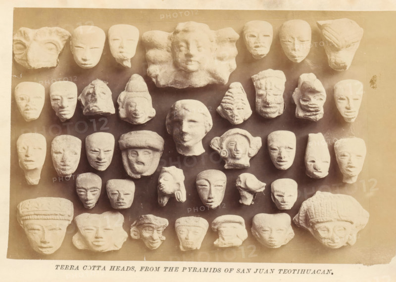 Terra cotta heads, from the pyramids of San Juan Teotihuacan, photograph, page, Mexico, c. 1870 - in or before 1880, photographer, North America, paper, albumen print, height 102 mm x width 155 mm, sculpture, head (human), A grid of small sculpted heads arranged against a rectangular backdrop, each head carved from a light-colored material with varied facial features and headgear, showing smooth and textured surfaces, some with rounded faces, some elongated, some partial or worn, and a few with pronounced brows, noses, or lips; the backdrop has a warm sepia tone and a narrow border around the edges, with a strip of paper visible below the backdrop.